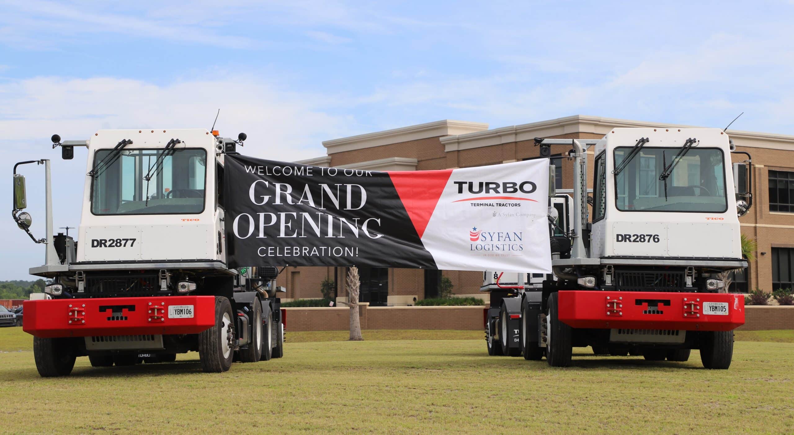 Two trucks hold a banner announcing the grand opening of Turbo's new Savannah office.